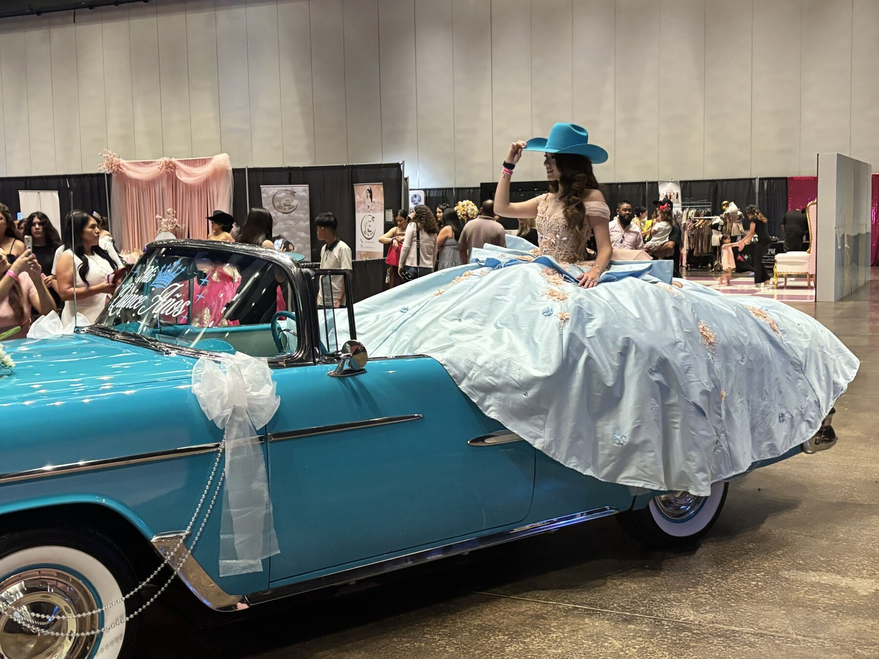 Young woman in a light-blue quinceañera gown and turquoise hat posing with Ole' Belle at the Quinceañera Expo